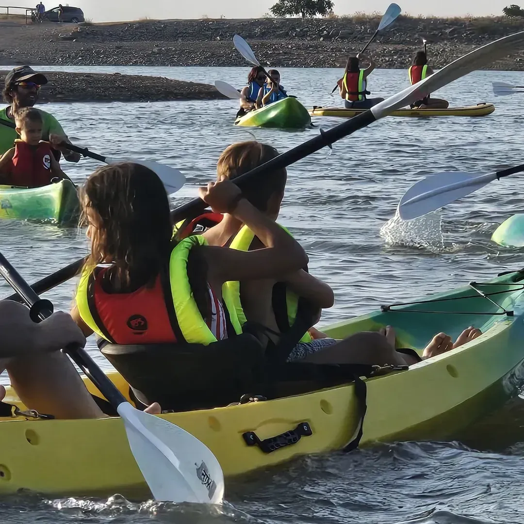 Gente haciendo kayak en el agua; algunos son niños que llevan chalecos salvavidas.