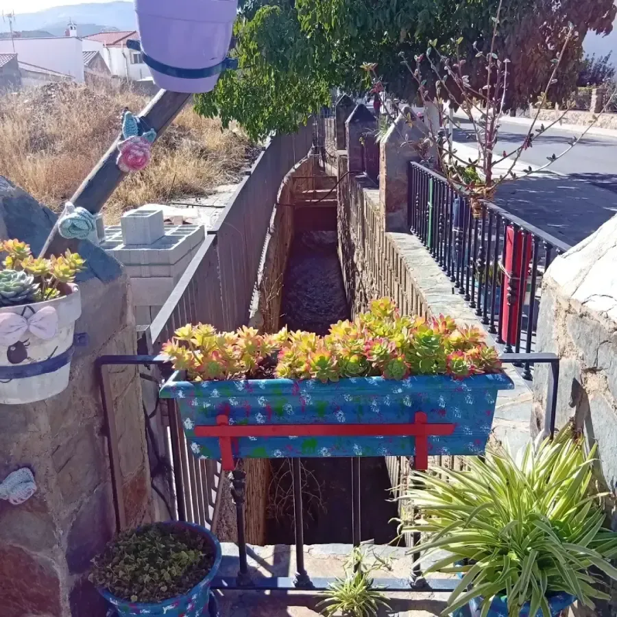 Canal de agua revestido de piedra con jardineras decorativas y barandilla. Suculentas y otras plantas aportan color.