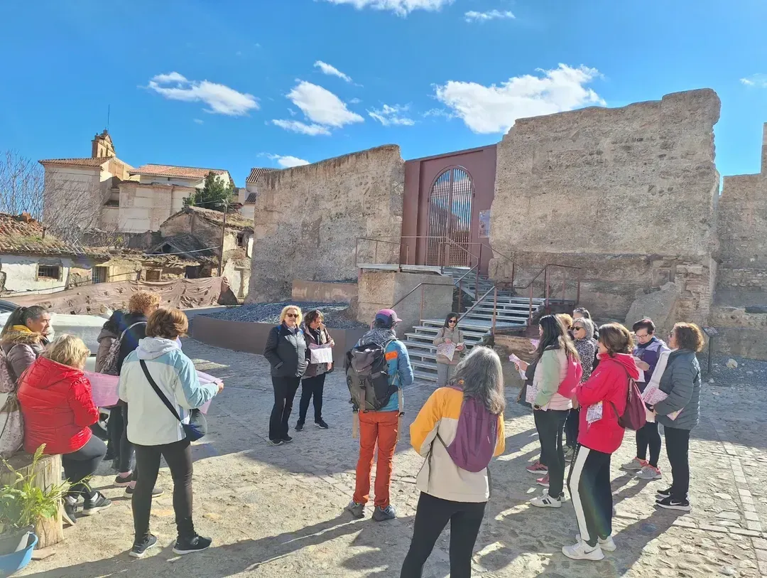 Grupo de personas en un recorrido observando antiguas ruinas de piedra bajo un cielo azul.