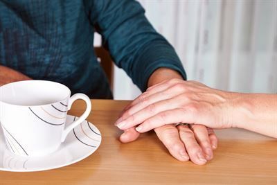 Eine Person hält die Hand einer anderen Person, während sie mit einer Tasse Kaffee an einem Tisch sitzt.