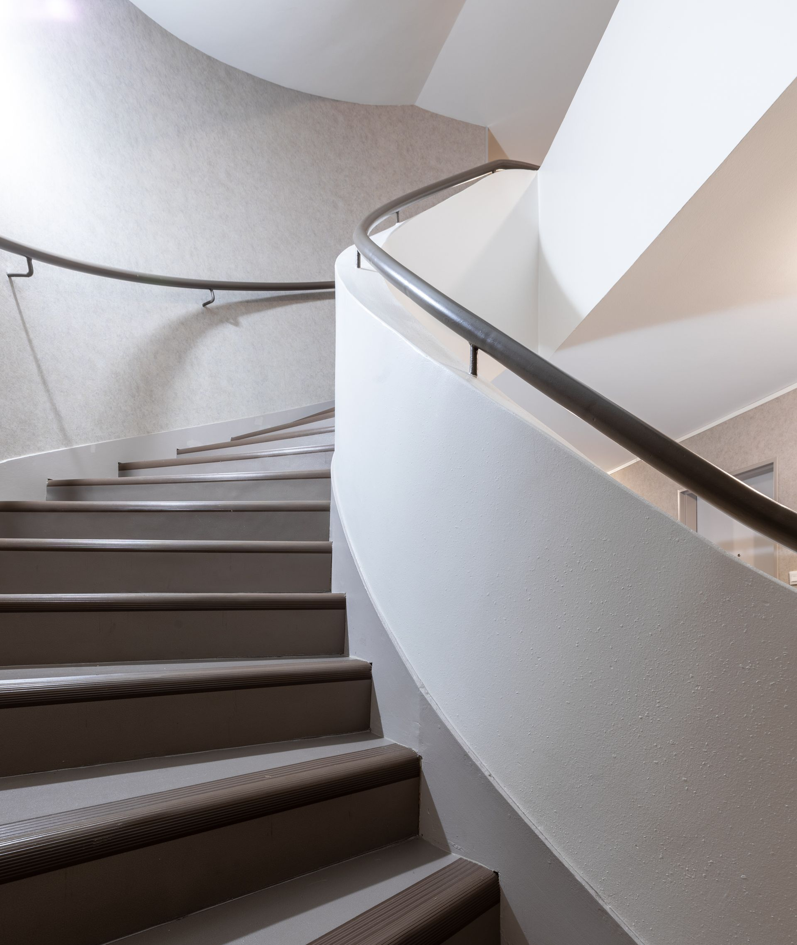 Un ouvrier du bâtiment, vêtu d'un équipement de sécurité, se tient sur un échafaudage en train de peindre un mur extérieur.