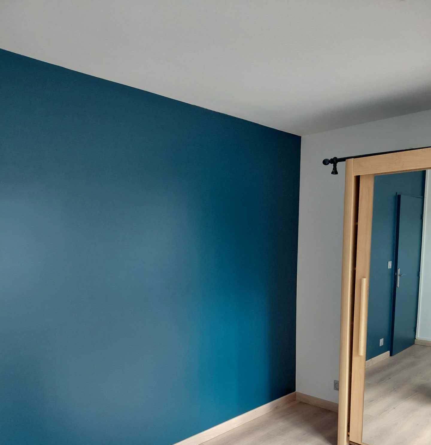 Une personne portant un gant gris utilise un rouleau pour appliquer de la peinture sur une façade.