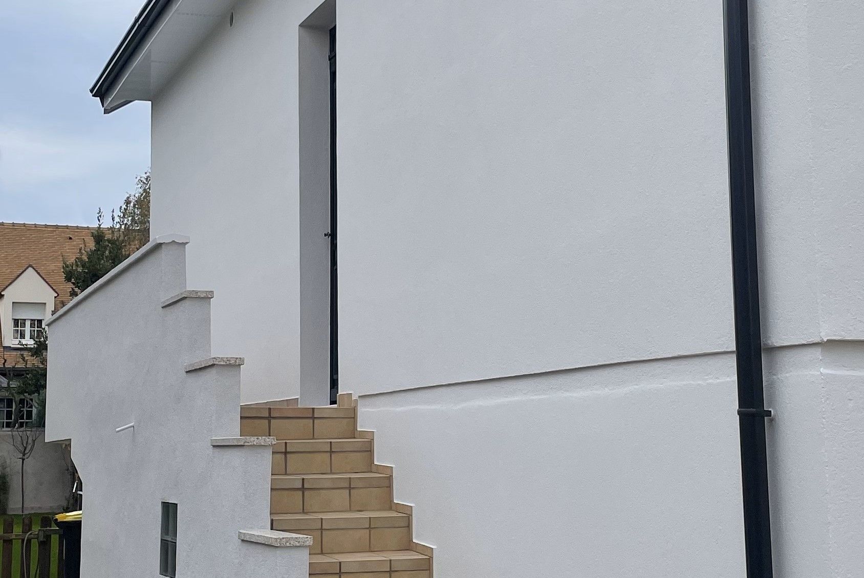 Un escalier extérieur carrelé de couleur beige mène à une porte blanche sur le côté d'une maison blanche.