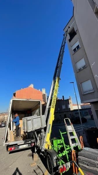 Camión con plataforma elevadora descargando cajas en un edificio de apartamentos en un día soleado.