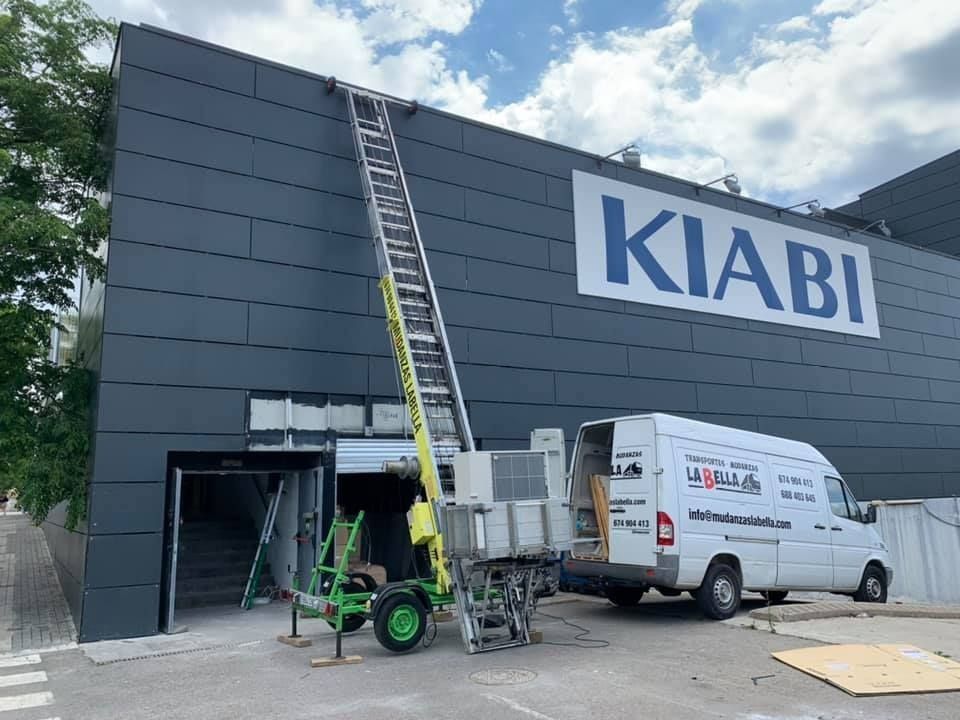 Exterior de una tienda KIABI con un elevador. Una furgoneta blanca está estacionada junto al edificio.