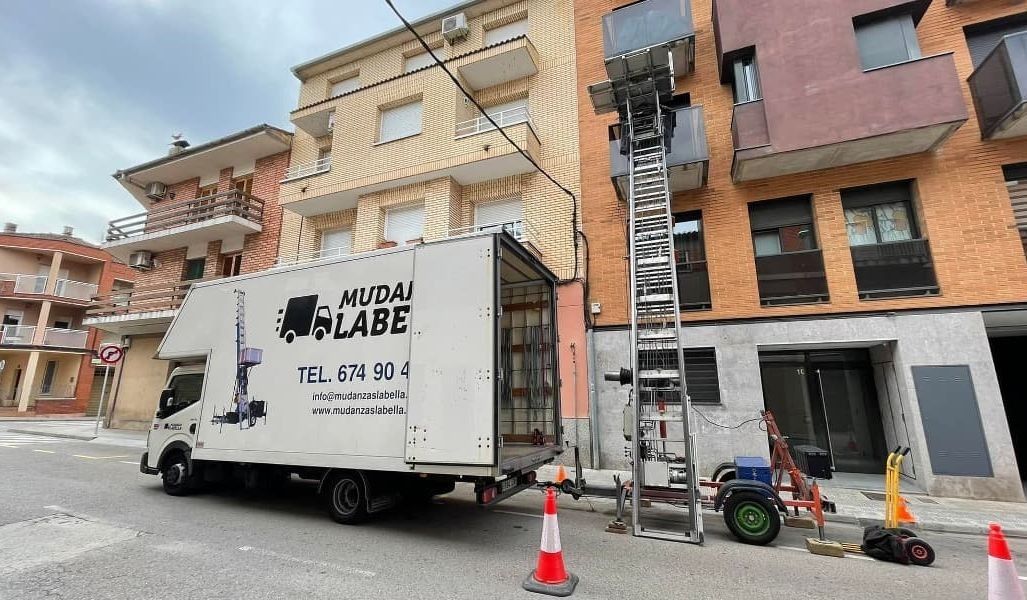 Camión de mudanzas con elevador, cargando muebles en un edificio.