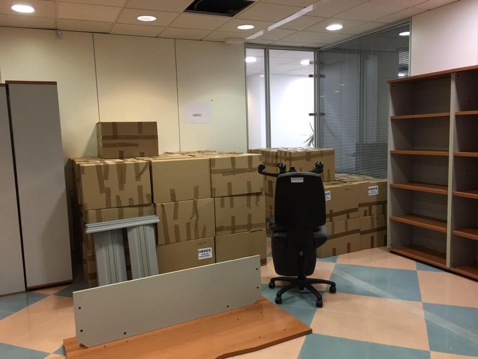 Oficina en remodelación; cajas apiladas, silla de oficina, estantes y materiales de construcción visibles.