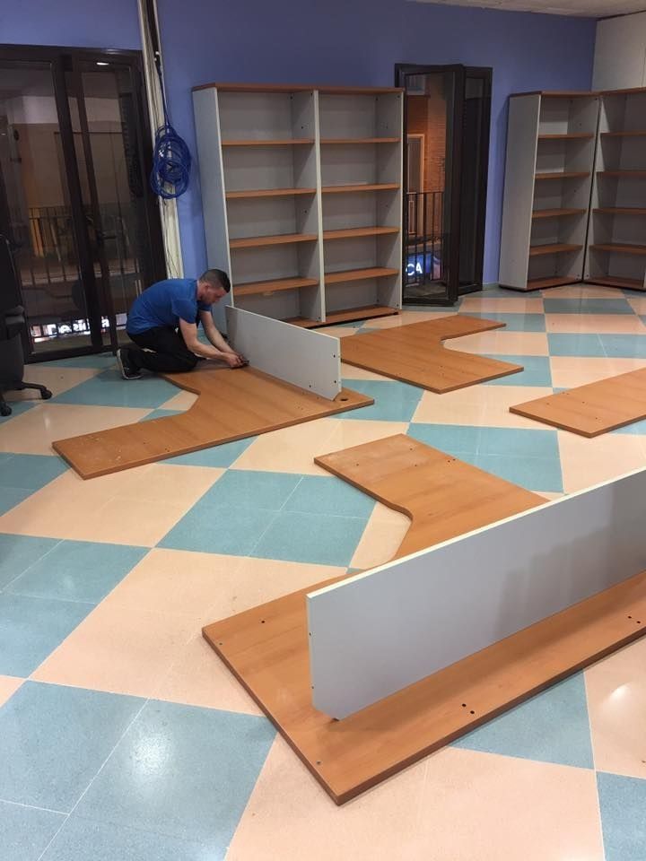Persona montando muebles en una habitación con estanterías y suelo a cuadros.