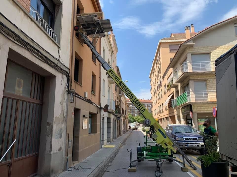 Un ascensor en movimiento se extiende hasta la ventana de un edificio en una calle estrecha con edificios a ambos lados.