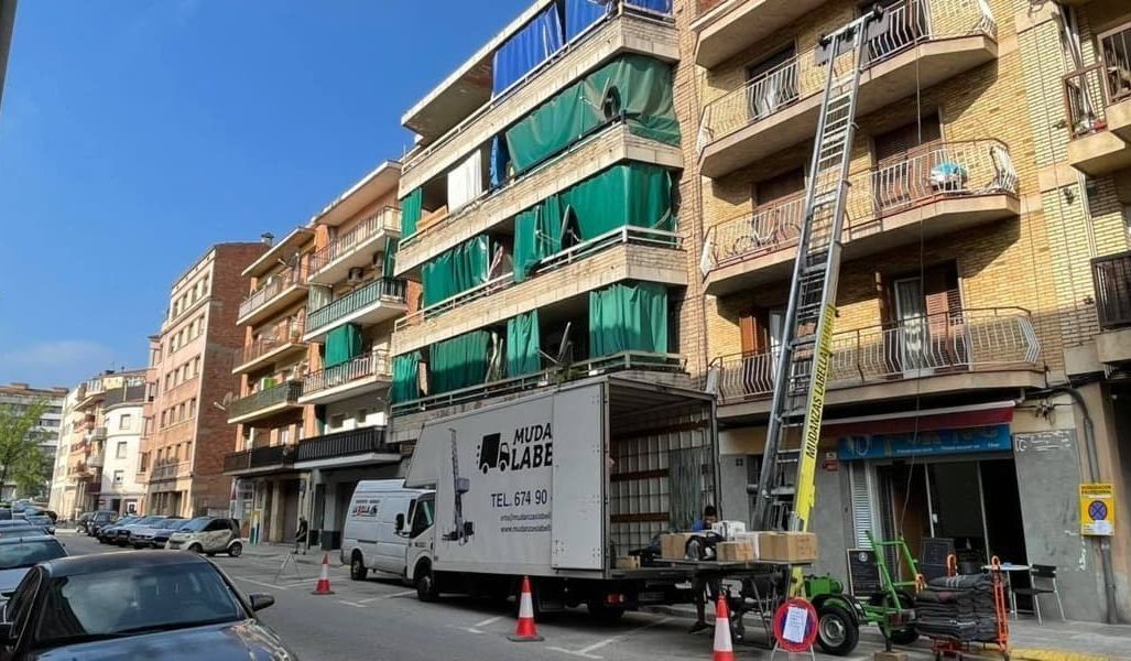 Camión de mudanzas con elevador descargando muebles de un edificio en una calle de la ciudad.