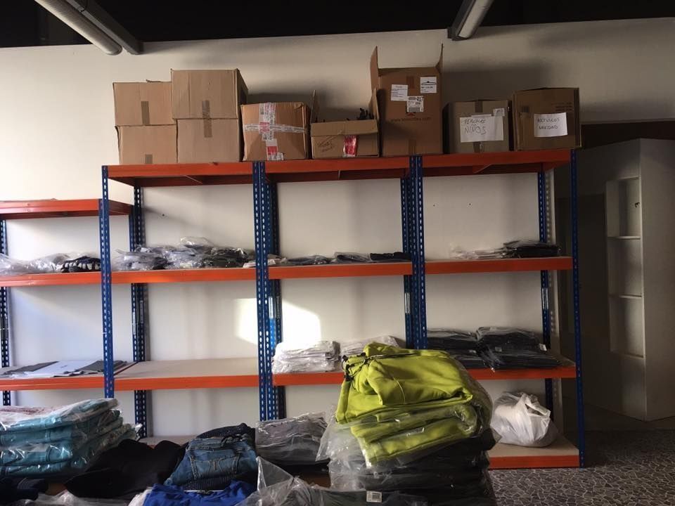 Estanterías de almacén con cajas arriba y ropa abajo. Azul, naranja y canela.