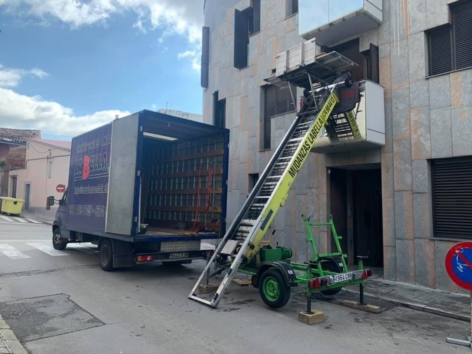 Camión de mudanzas y ascensor descargando artículos del balcón de un edificio.