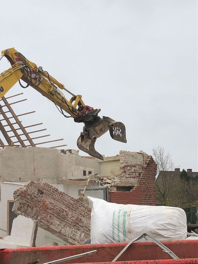 Ein gelber Bagger zerstört ein Backsteingebäude