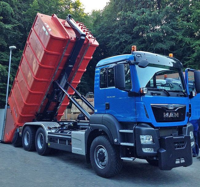 Ein blauer LKW mit einem roten Müllcontainer auf der Rückseite