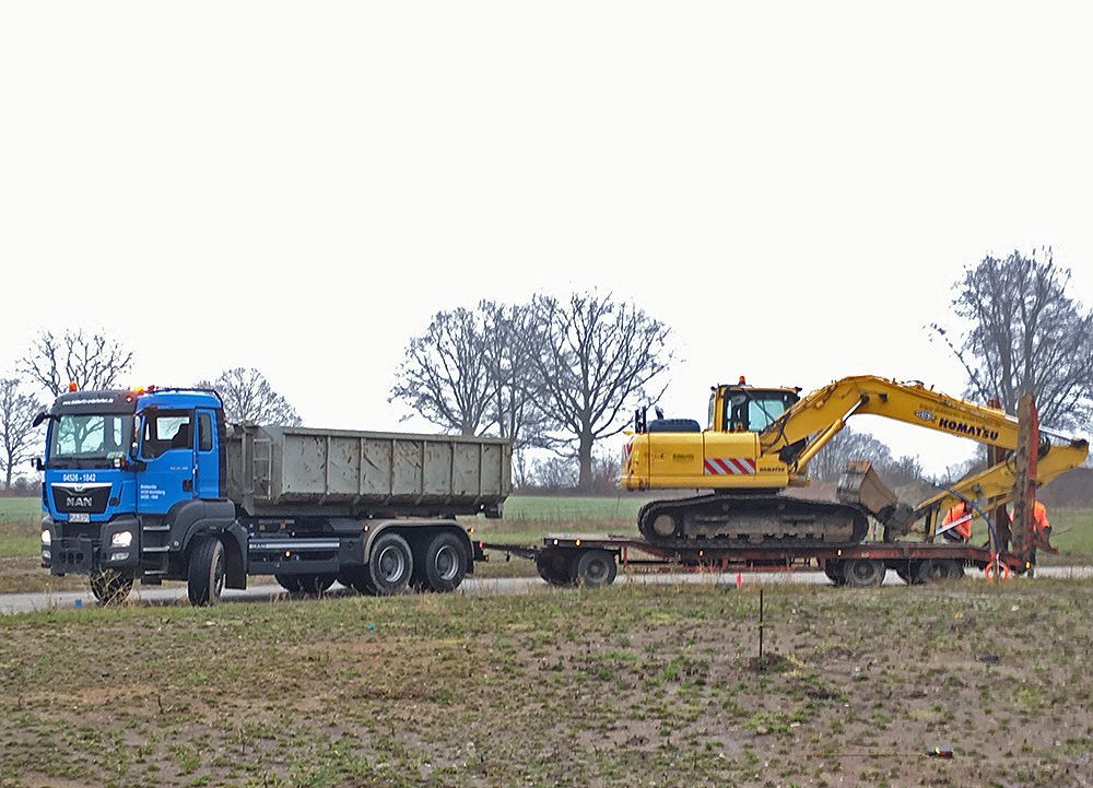 Ein blauer LKW zieht einen gelben Bagger auf einem Anhänger.