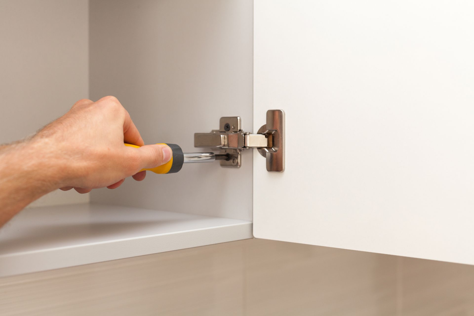 Una persona está arreglando la puerta de un armario con un destornillador.