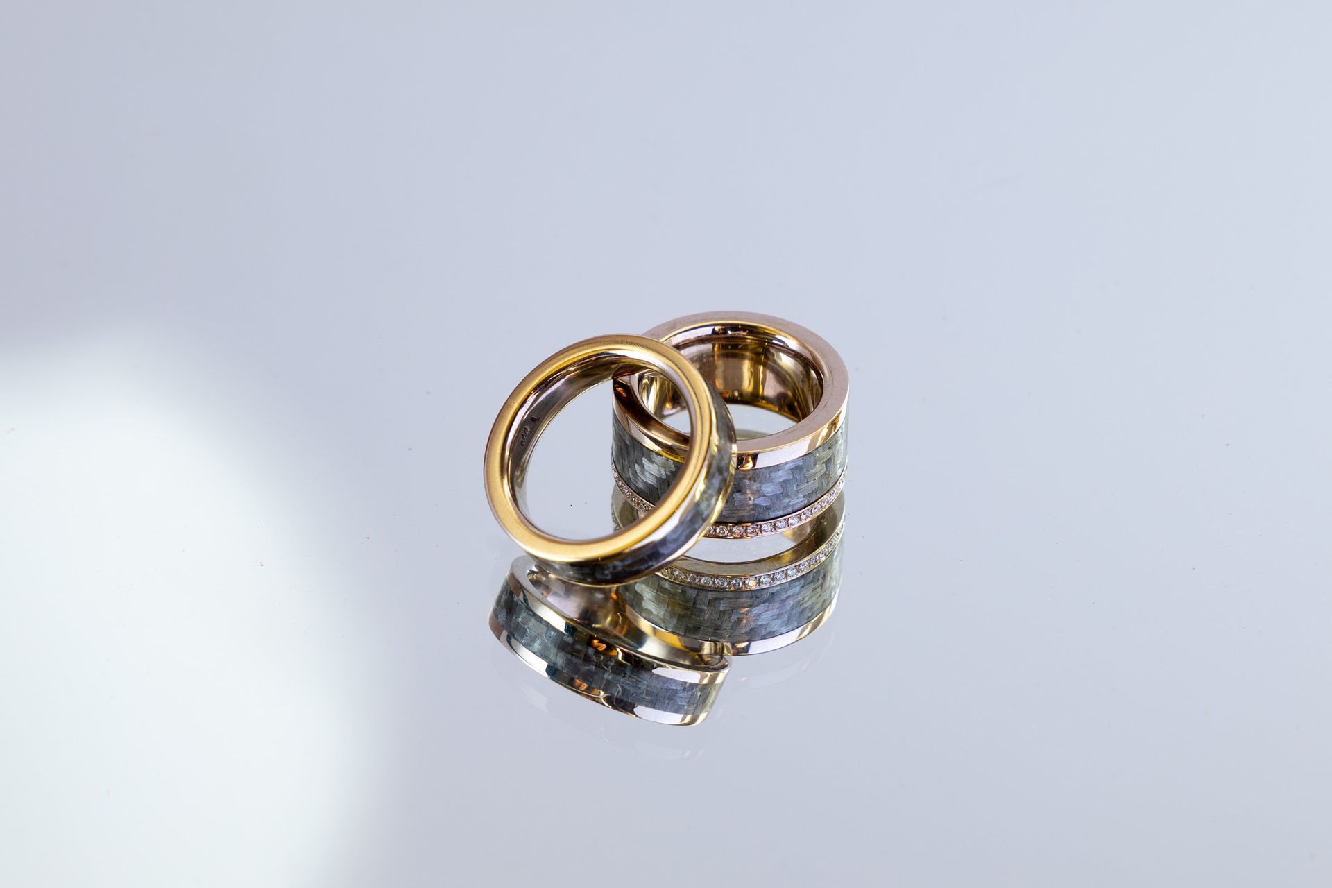 Zwei goldene Ringe mit einem silbernen Band ruhen auf einer reflektierenden Oberfläche