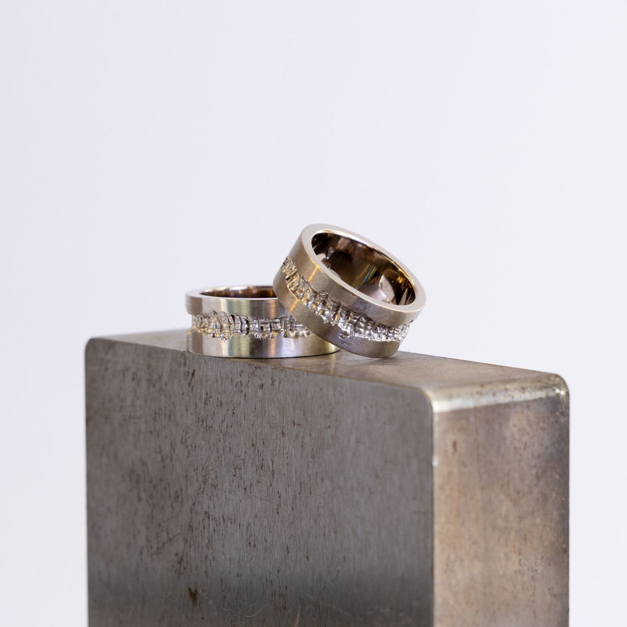 Zwei silberne Ringe lehnen an einem grauen Metallblock vor hellem Hintergrund
