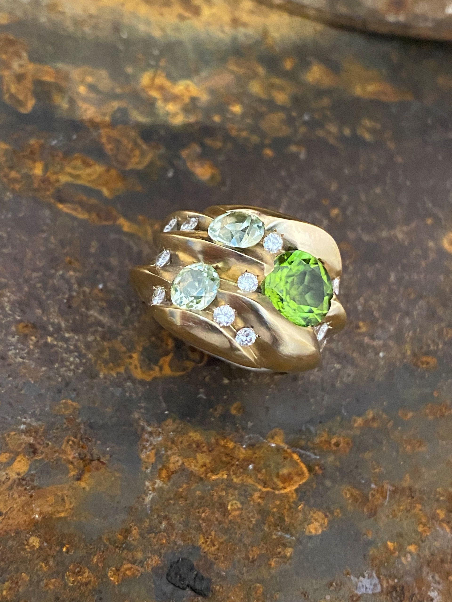 Goldring mit grünen und klaren Edelsteinen auf strukturiertem braunem Untergrund