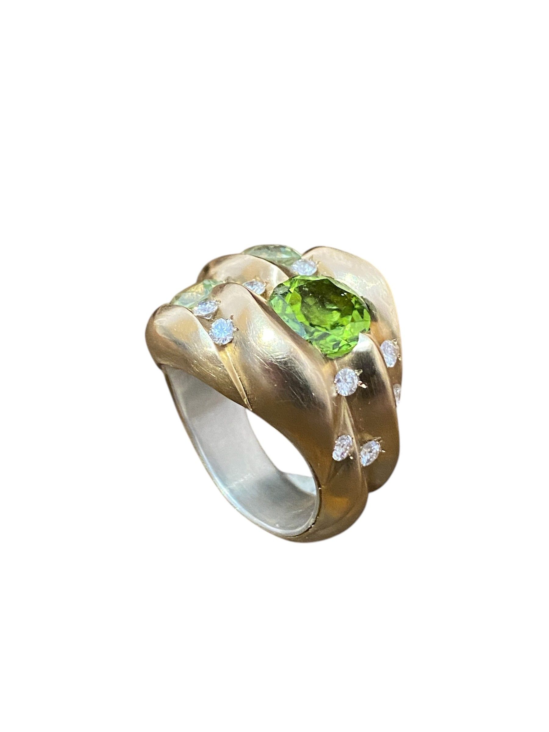 Goldring mit einem leuchtend grünen Edelstein und kleinen klaren Steinen auf weißem Grund