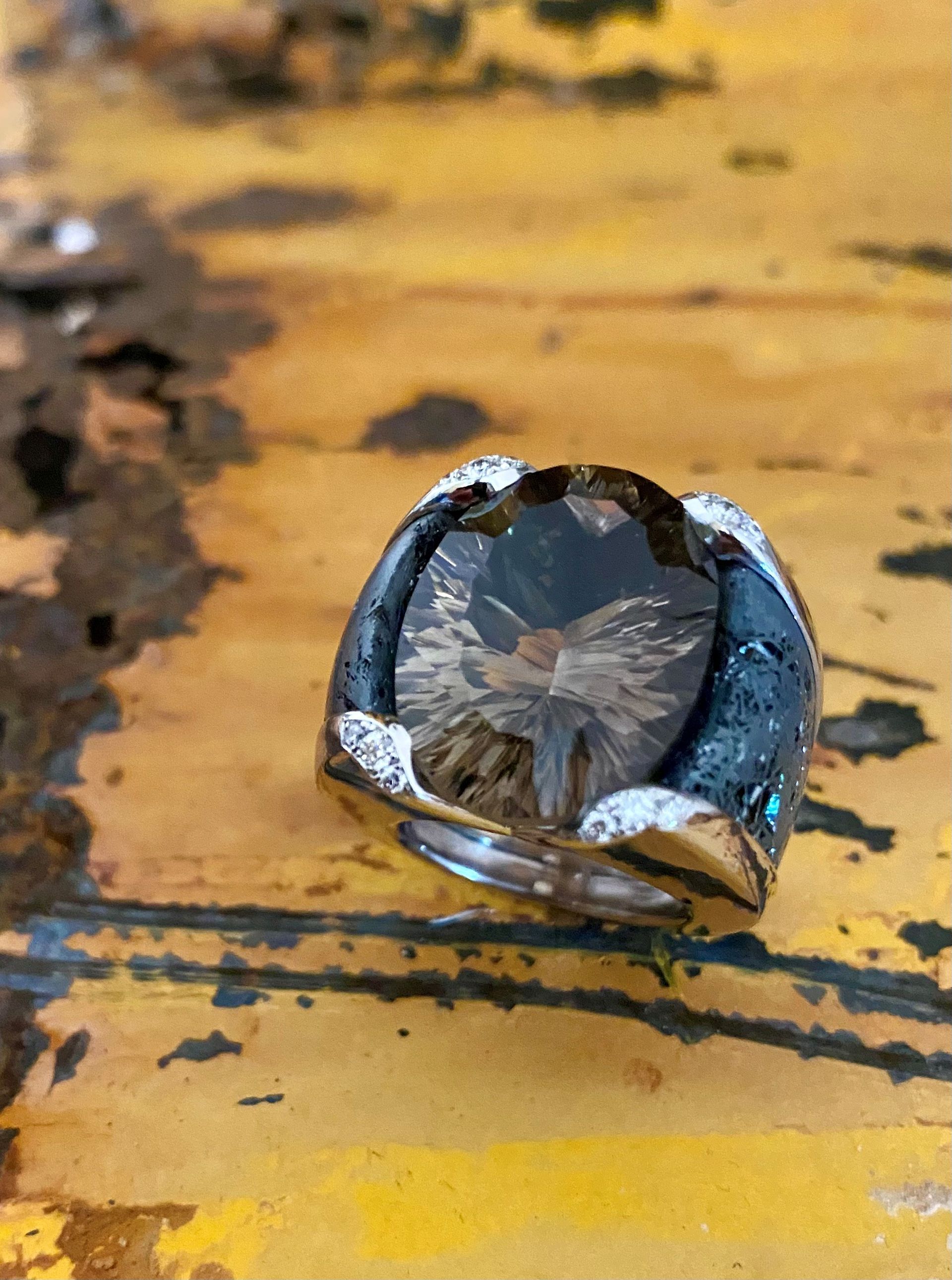 Kleiner metallischer Gegenstand mit durchsichtigem Zentrum, der auf einer gelb lackierten Oberfläche mit dunklen Rissen liegt.