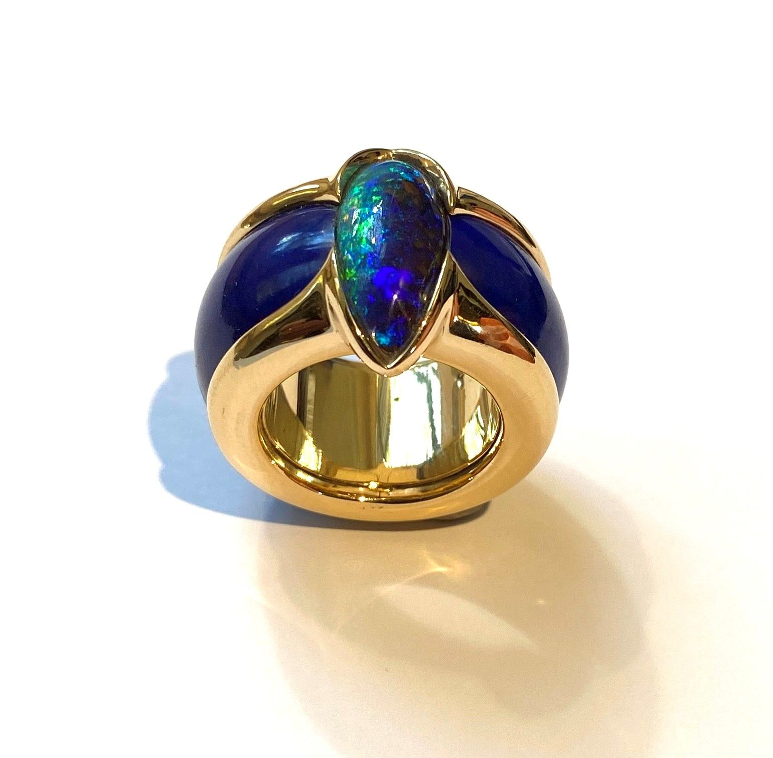 Goldring mit blauen und irisierenden Edelsteinakzenten auf weißem Hintergrund