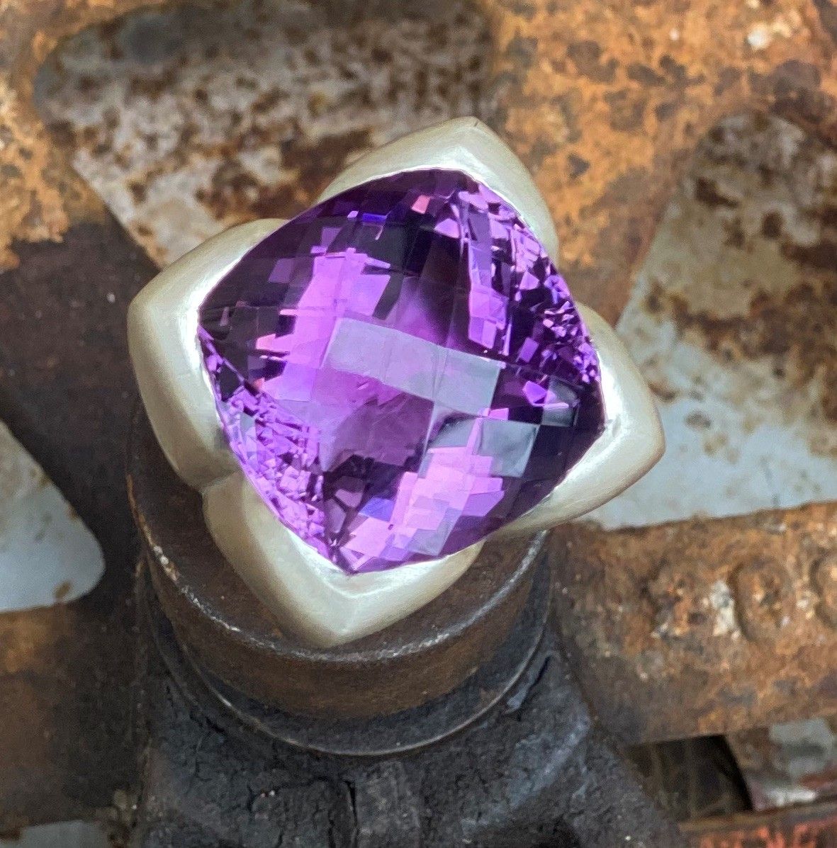 Violetter, facettierter Edelstein in einer silbernen Ringfassung auf einer rostigen Metalloberfläche