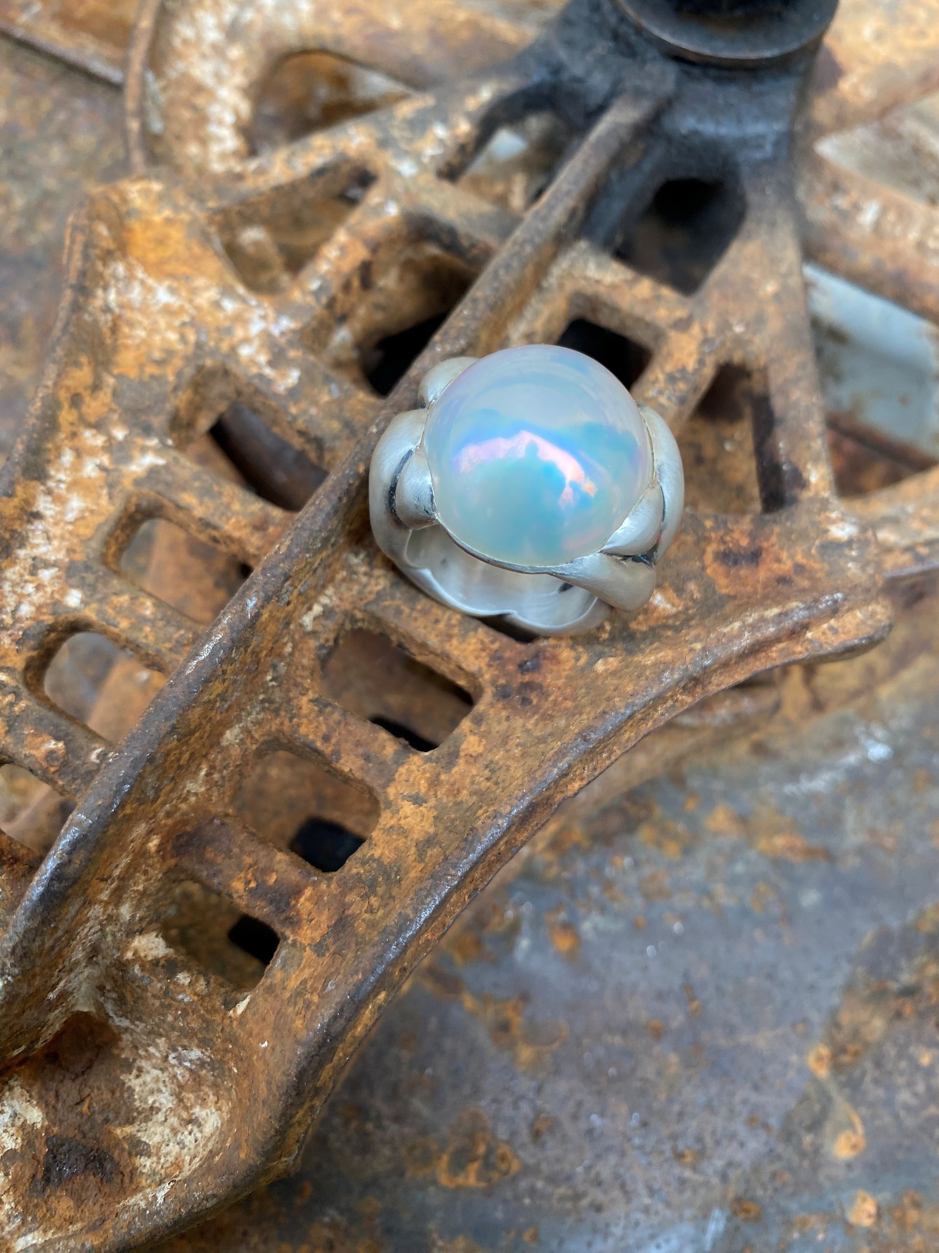Nahaufnahme eines blauen Opals, der in einen Silberring auf einer rostigen Metalloberfläche gefasst ist