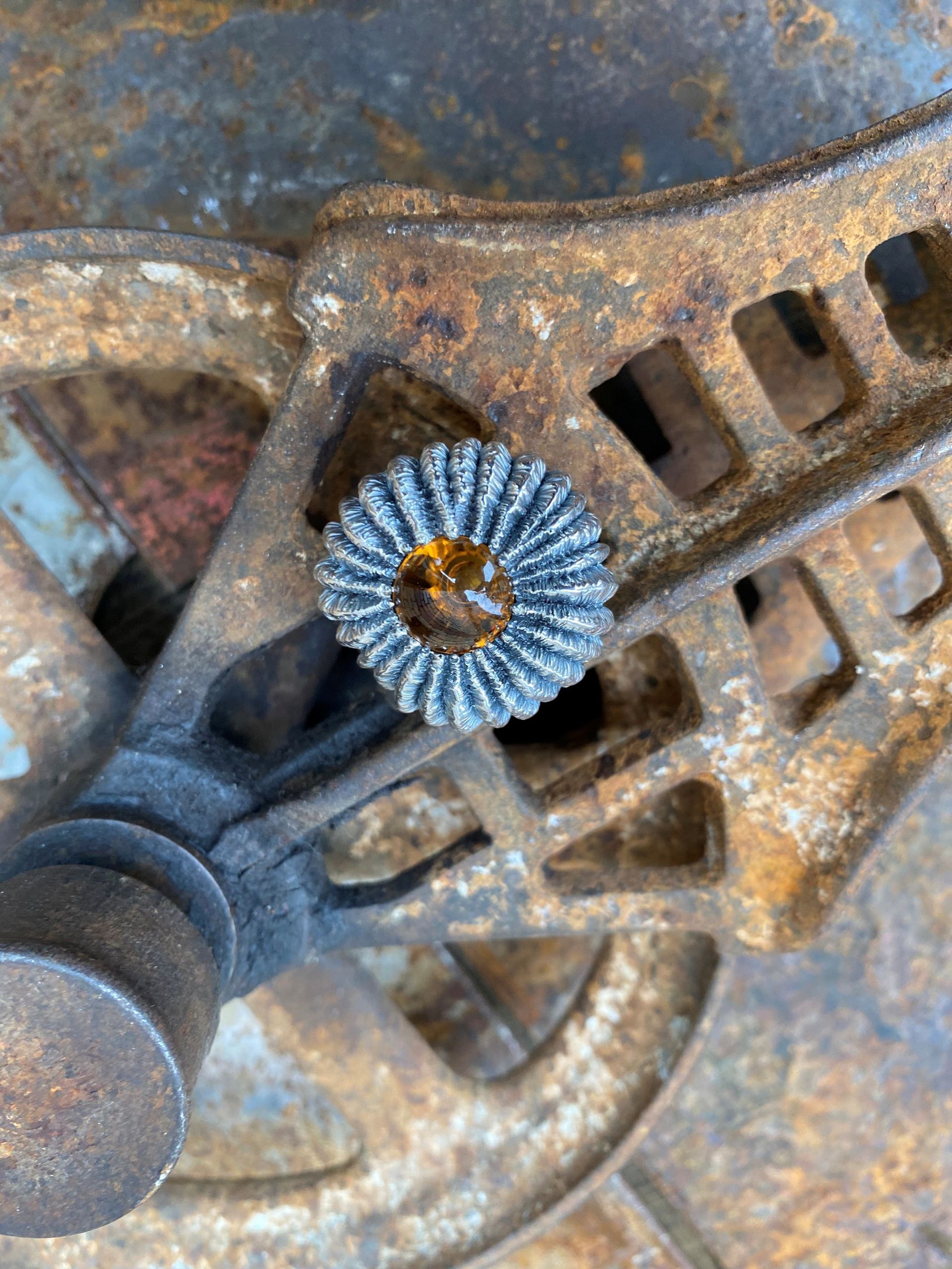 Nahaufnahme einer verrosteten, blau-braunen, blumenförmigen Metallschraube auf einer industriellen Oberfläche.