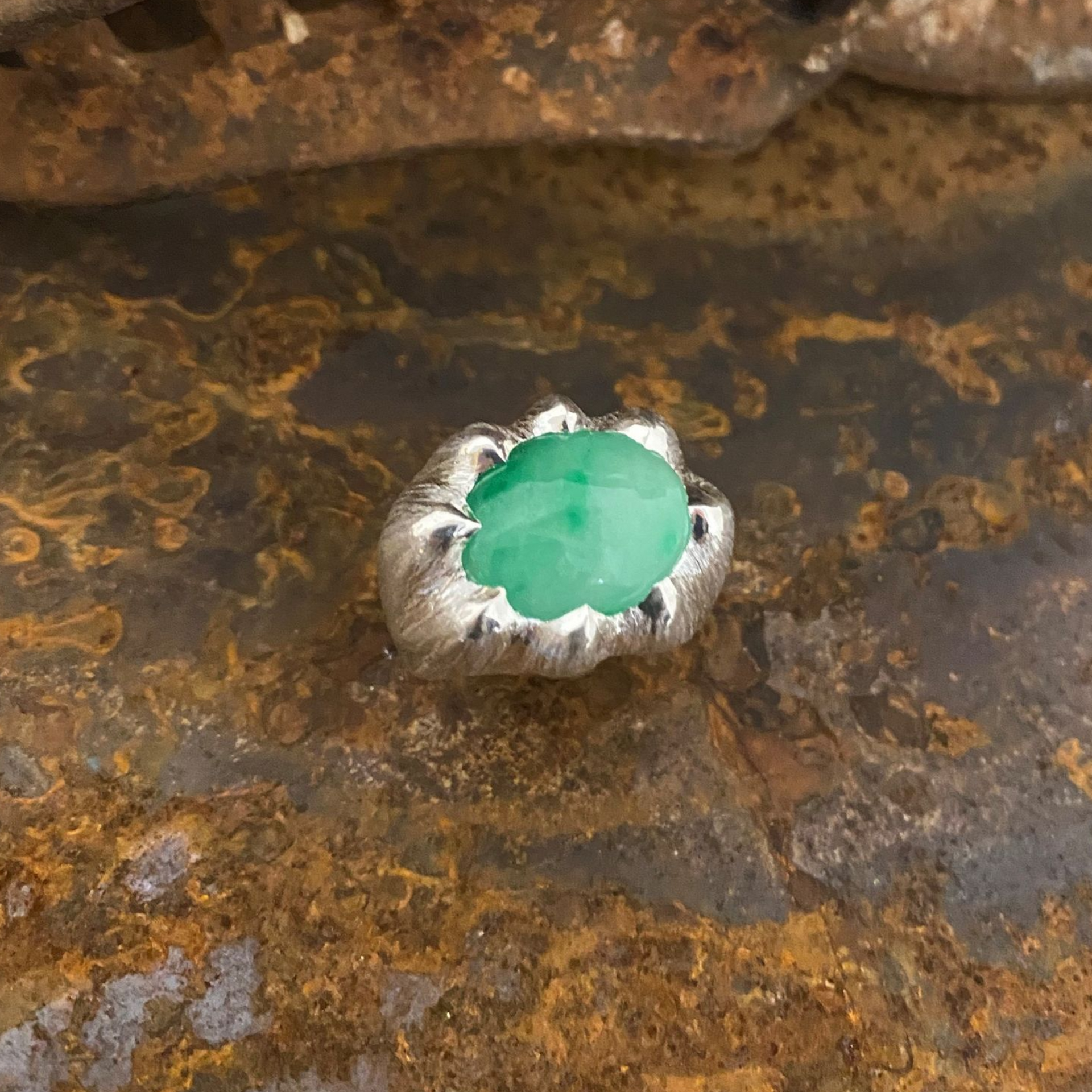 Grüner Edelstein in Silberfassung auf rostiger Metalloberfläche
