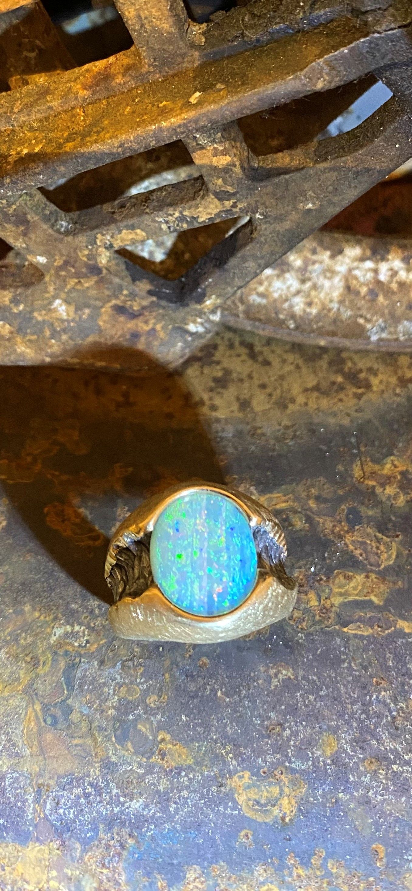 Goldring mit einem blauen Opalstein, der auf einer rostigen Metalloberfläche ruht.