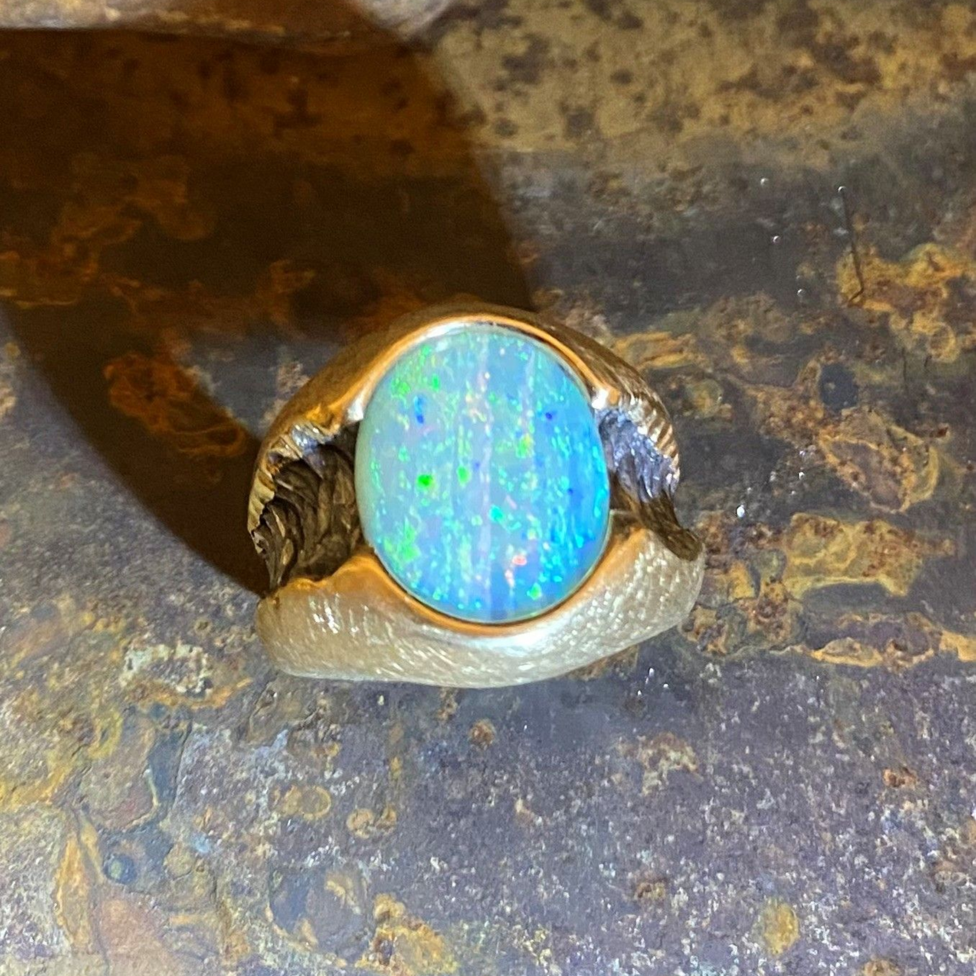 Nahaufnahme eines Goldrings mit einem runden blauen Opalstein auf dunkler Metalloberfläche