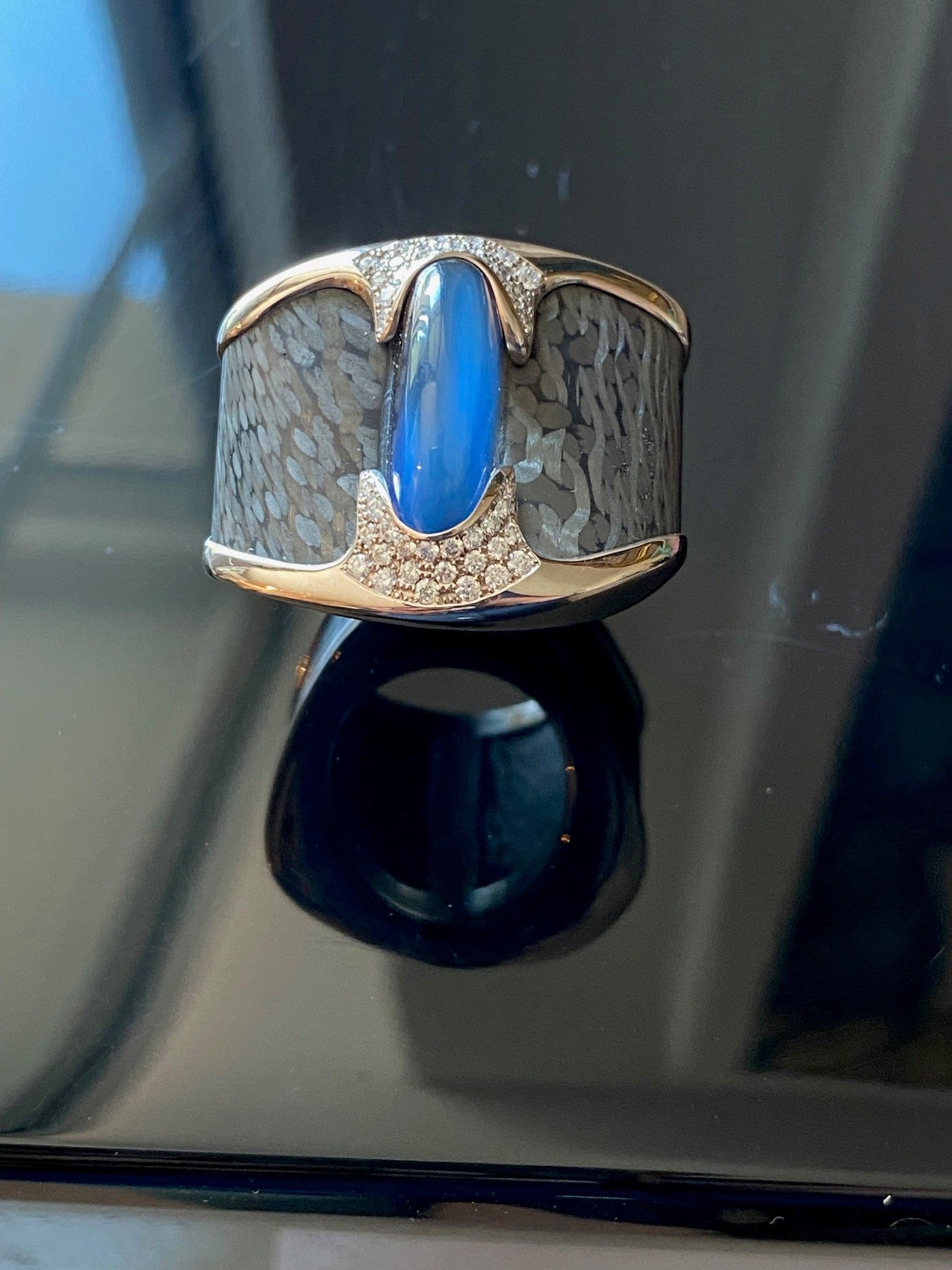 Nahaufnahme eines silbernen Rings mit einem blauen Mittelstein und einem schwarzen Ringband darunter.