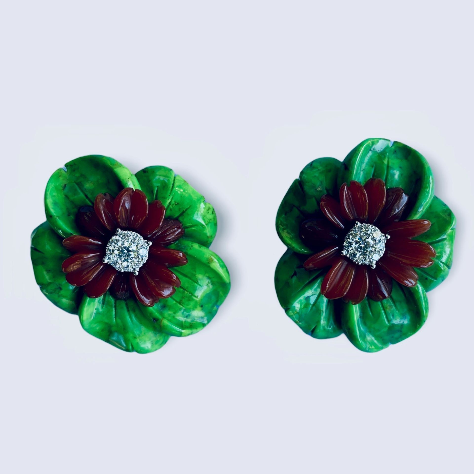 Paar grüne und bordeauxrote Blumenohrringe mit silbernen Zentren auf hellem Hintergrund