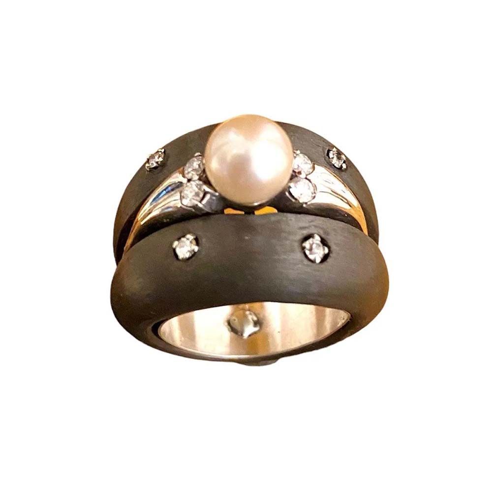 Goldring mit einer Perle als Mittelstück und kleinen Diamanten auf einem dunklen Ring, freigestellt auf weißem Hintergrund.