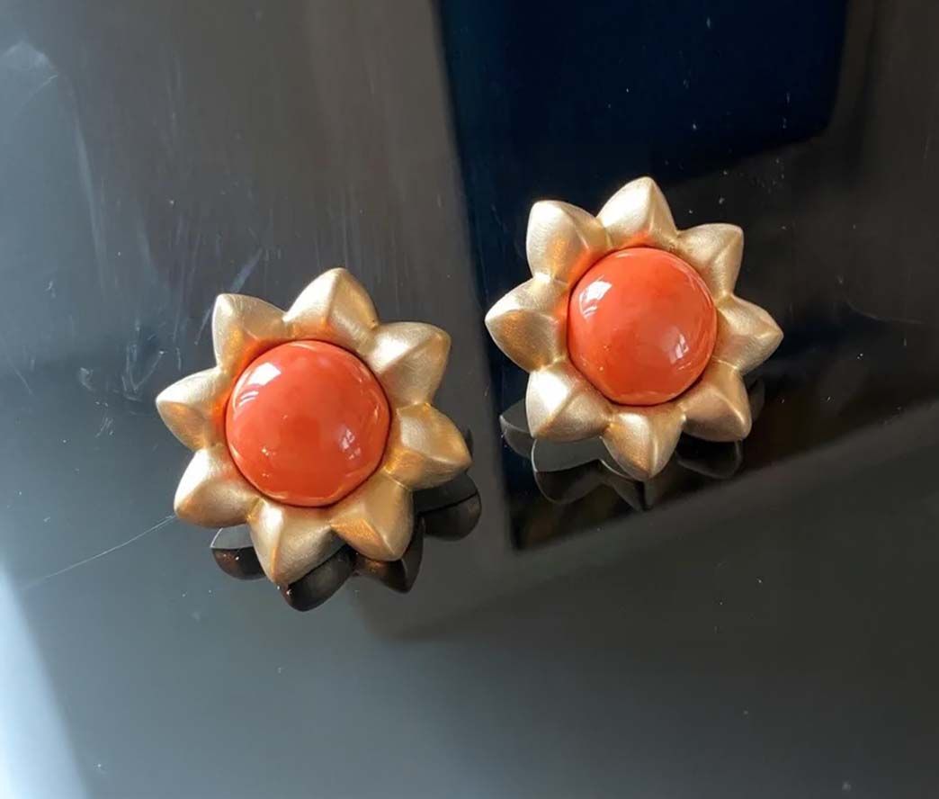 Ein Paar orange-goldene, blütenförmige Ohrringe auf dunkler Oberfläche