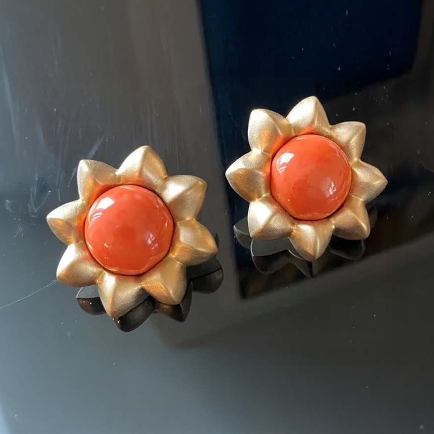 Paar goldene, blütenförmige Ohrringe mit orangefarbenen Zentren auf dunklem Untergrund