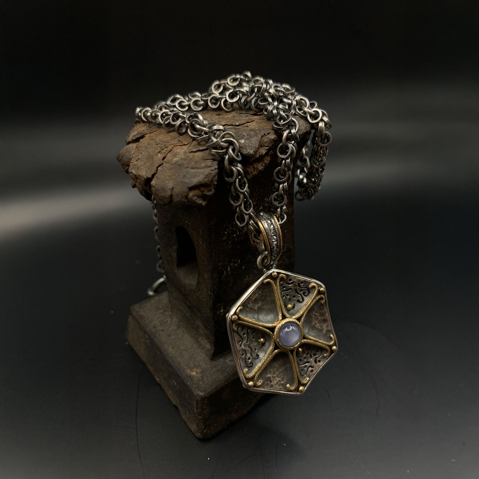 Rustikale Schmuckbüste aus Holz mit silberner Kette und geometrischem Goldanhänger auf dunklem Hintergrund