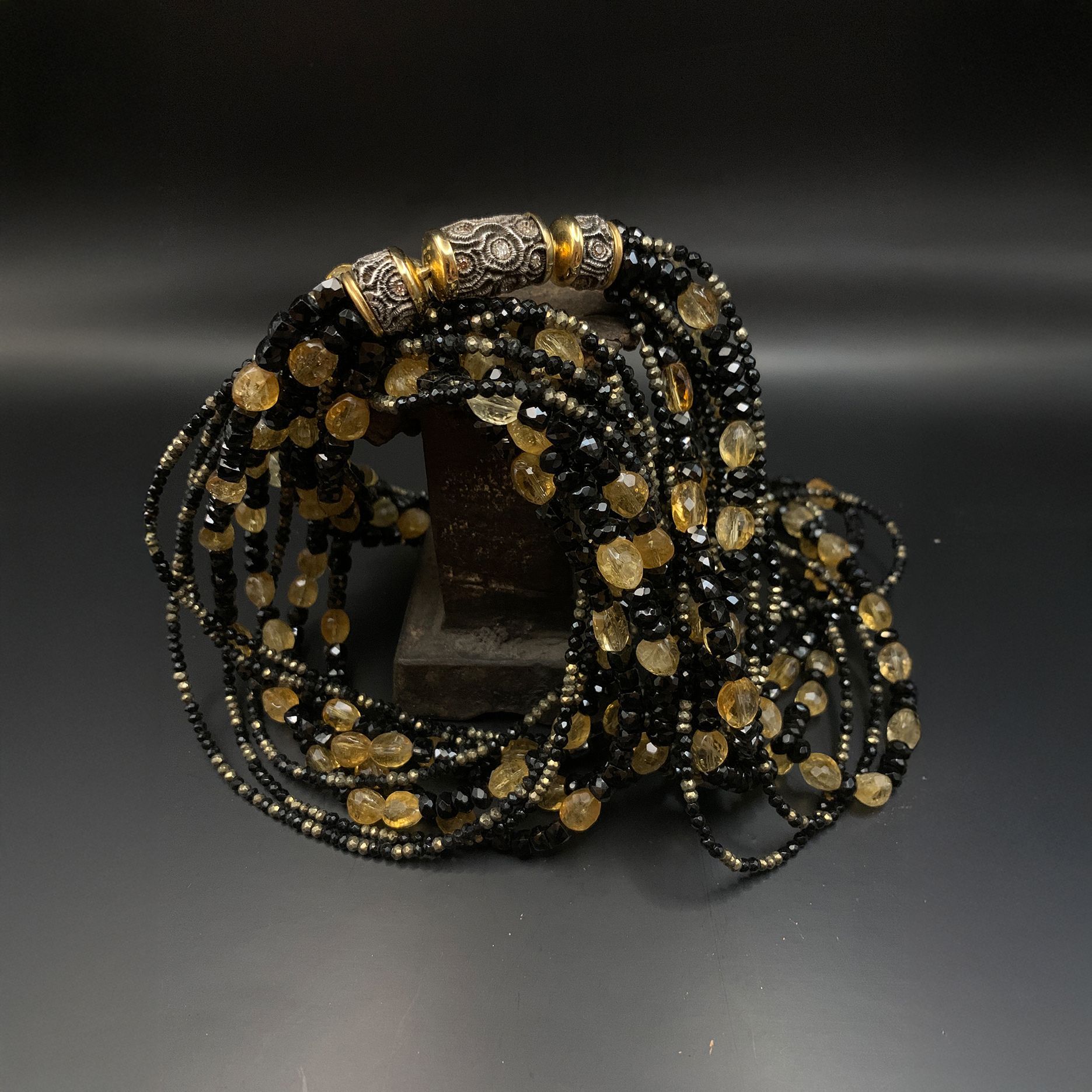 Schwarzes und goldenes, gewickeltes Perlenarmband auf dunklem Hintergrund