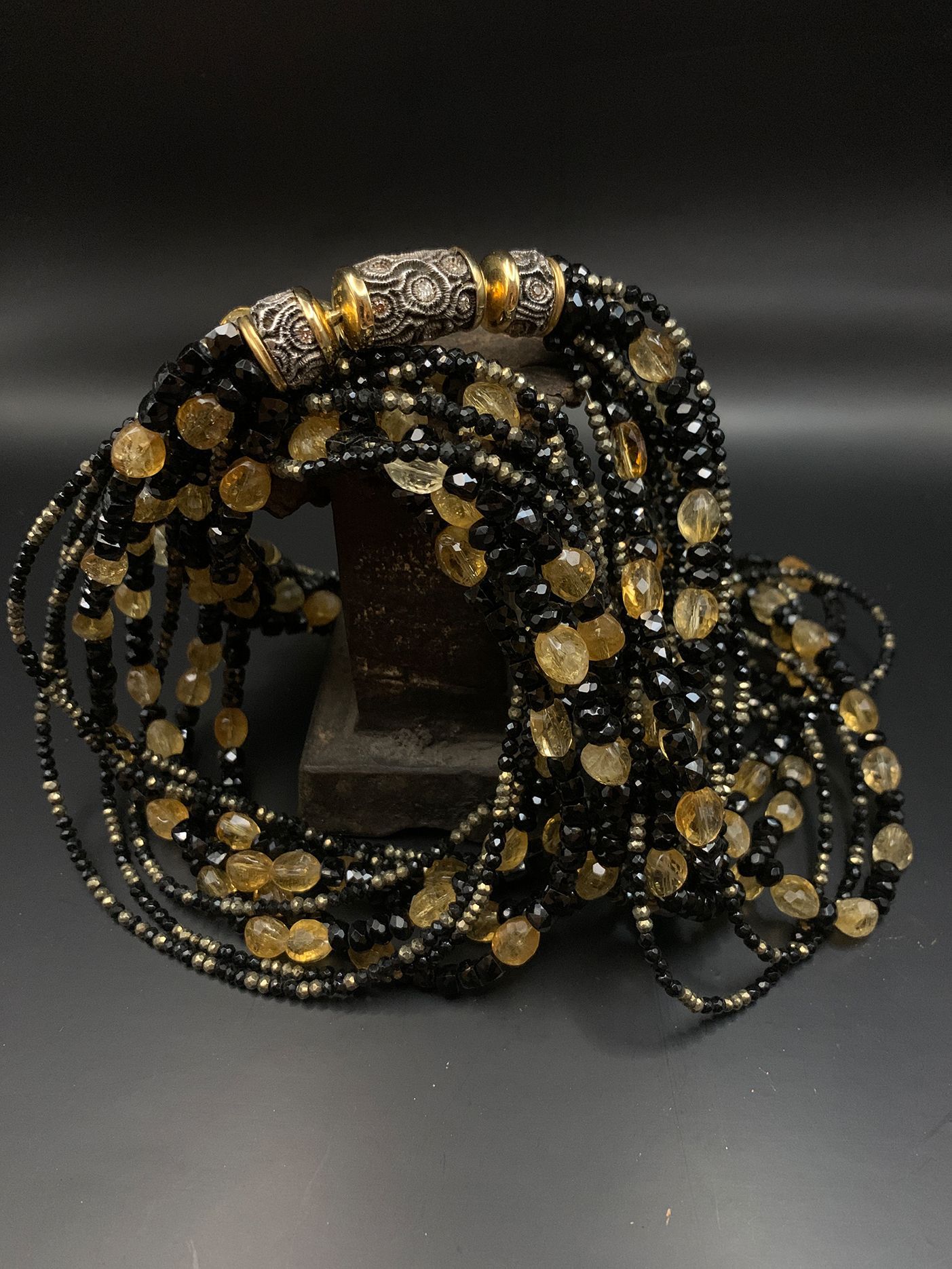 Schwarze und goldene Perlenspiralen mit Metallscheiben, angeordnet wie eine dekorative Halskette oder ein Kopfschmuck.