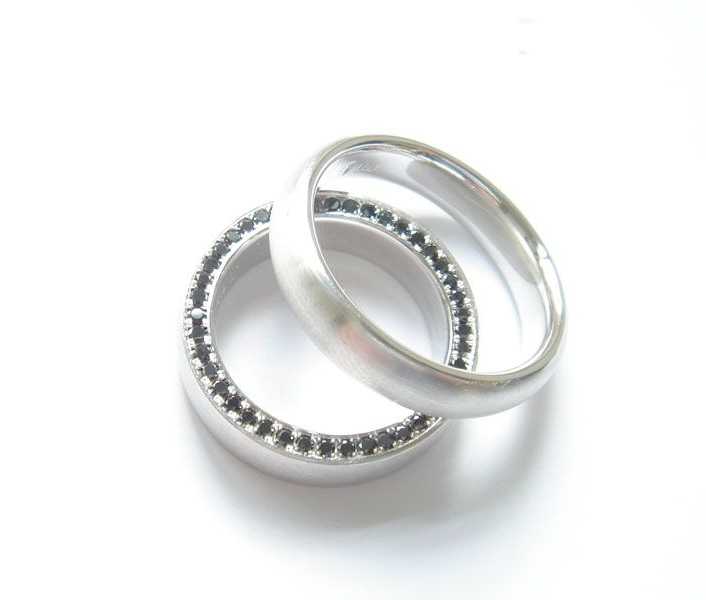 Zwei silberne Ringe auf weißem Grund, einer davon mit kleinen Steinen am Ringband
