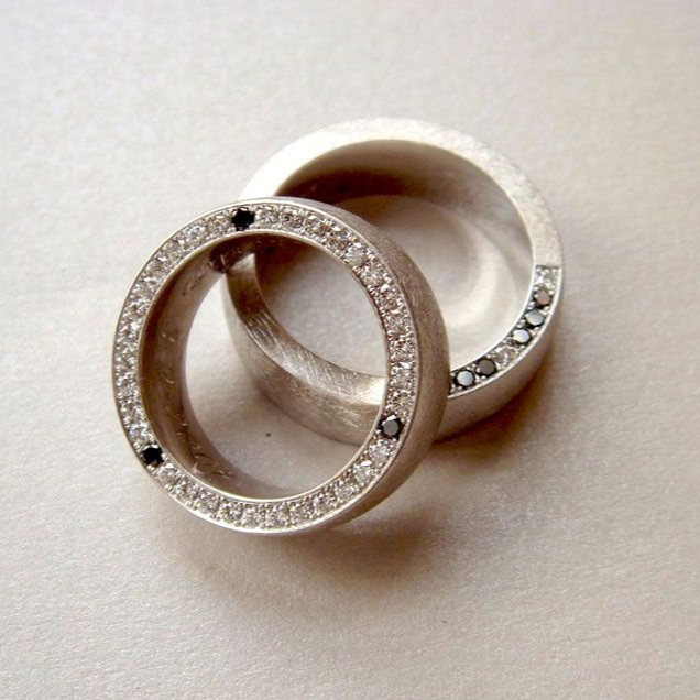 Zwei silberne Ringe mit kleinen Diamanten überlappen sich auf hellem Hintergrund.