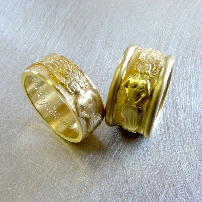 Zwei goldfarbene Ringe mit erhabenen Flächen, die auf einer hellgrauen Oberfläche ruhen.