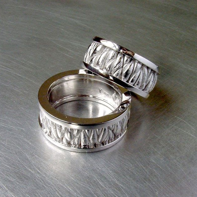 Zwei silberne, gravierte Ringe auf einer gebürsteten Metalloberfläche.