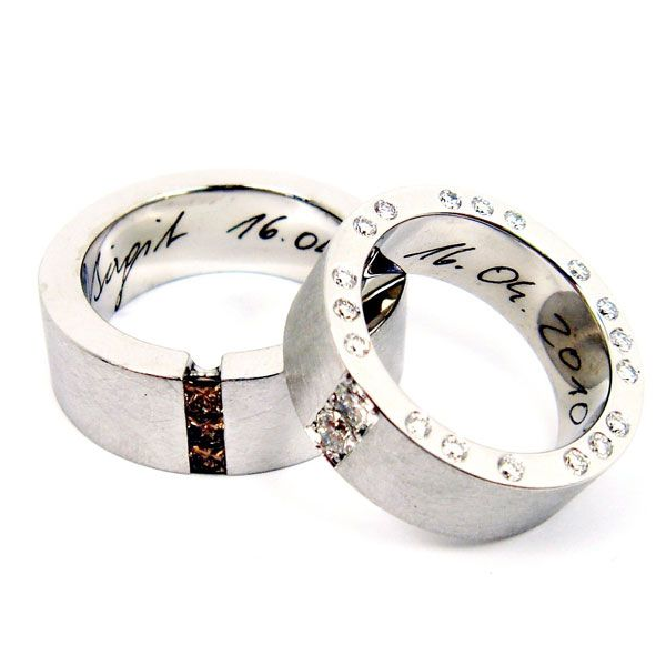 Zwei silberne Ringe mit eingraviertem Text, einer mit einer Reihe kleiner, klarer Steine und einer mit einem Einlegeelement
