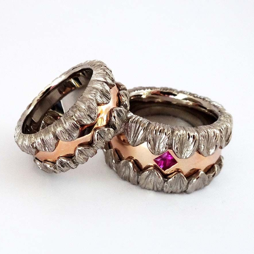 Drei silber- und goldfarbene Ringe mit Struktur, einer davon mit einem kleinen rosa Edelstein