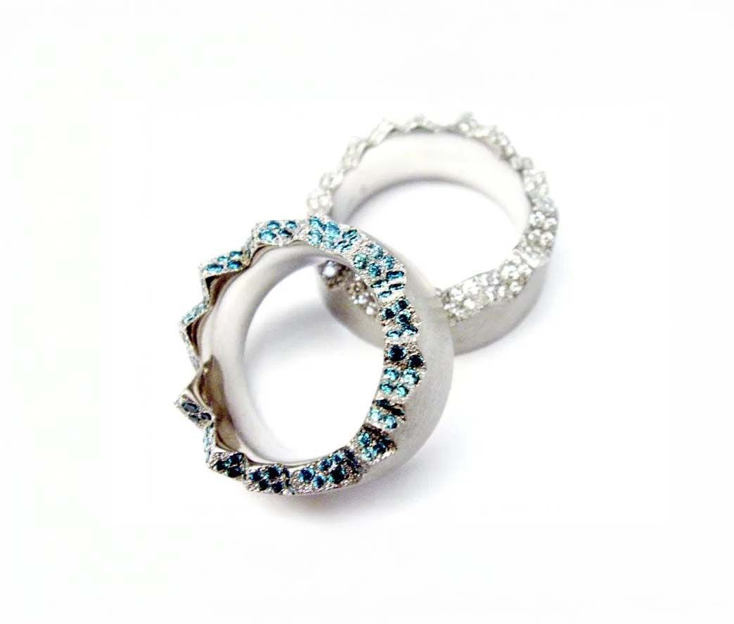 Zwei silberne Ringe mit kleinen blauen und klaren Steinen auf weißem Hintergrund
