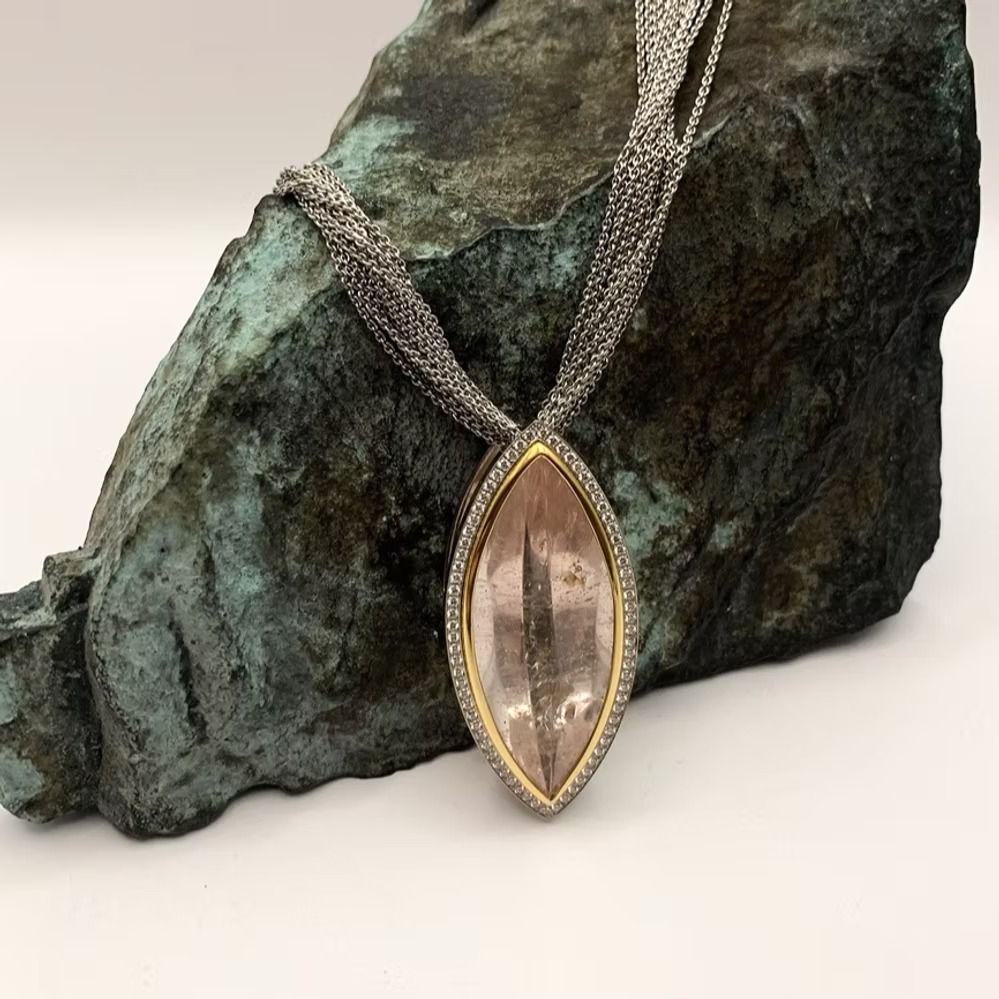 Halskette mit rosafarbenem Edelsteinanhänger vor einem strukturierten grün-grauen Gestein.