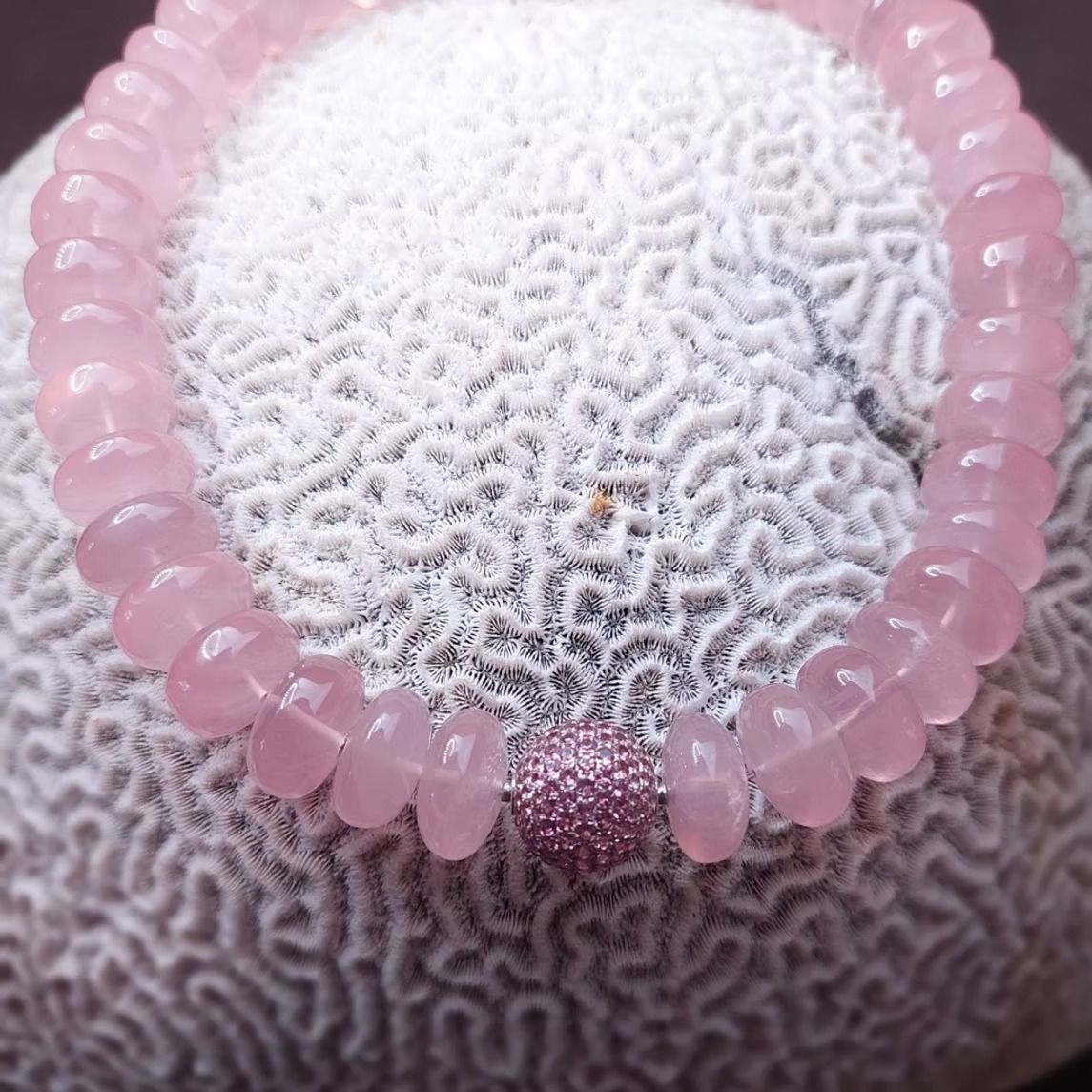 Armband aus rosa Rosenquarzperlen auf weißer, strukturierter Oberfläche.