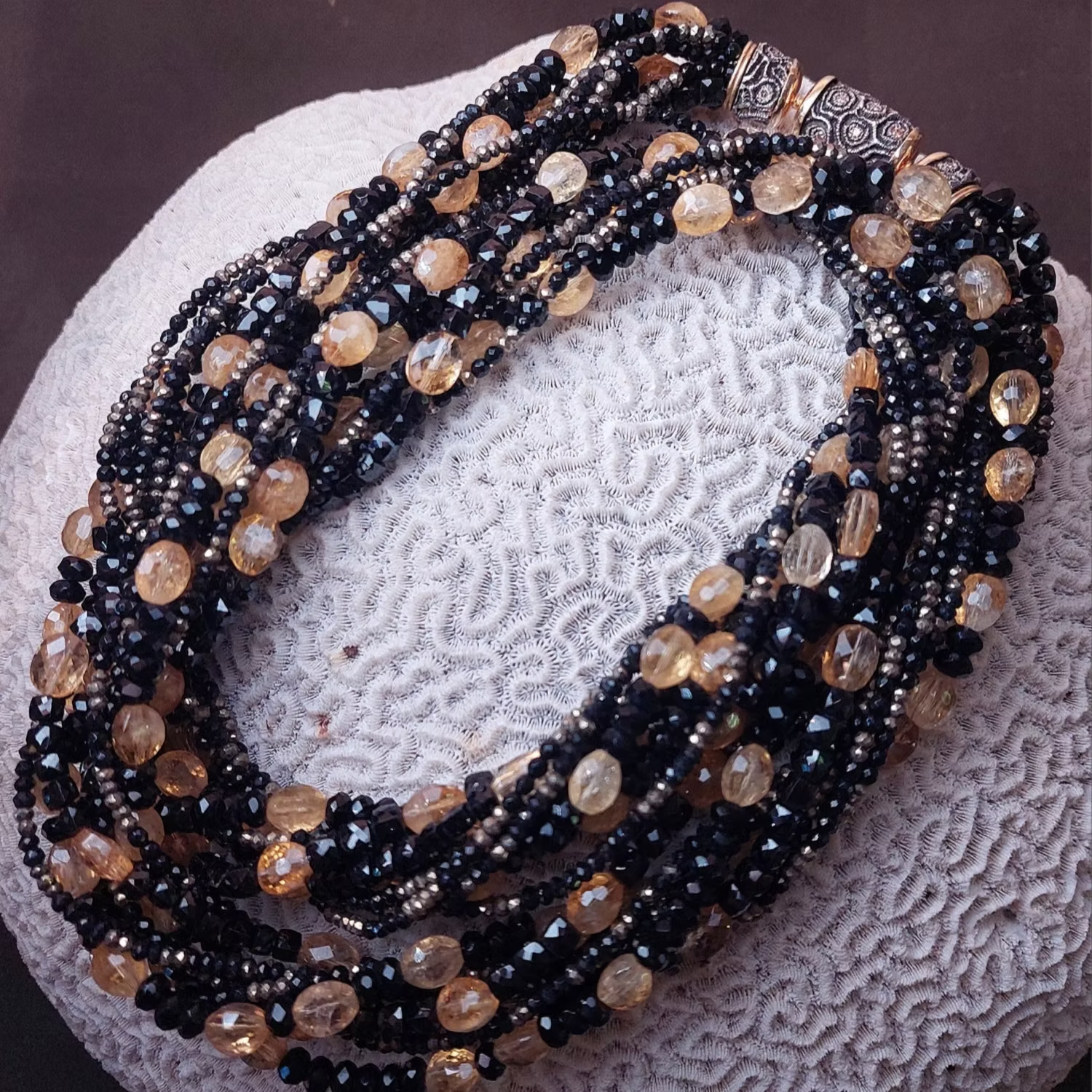 Mehrsträngige Halskette mit schwarzen und gelben Perlen, die auf einer weißen, strukturierten Oberfläche ruht.